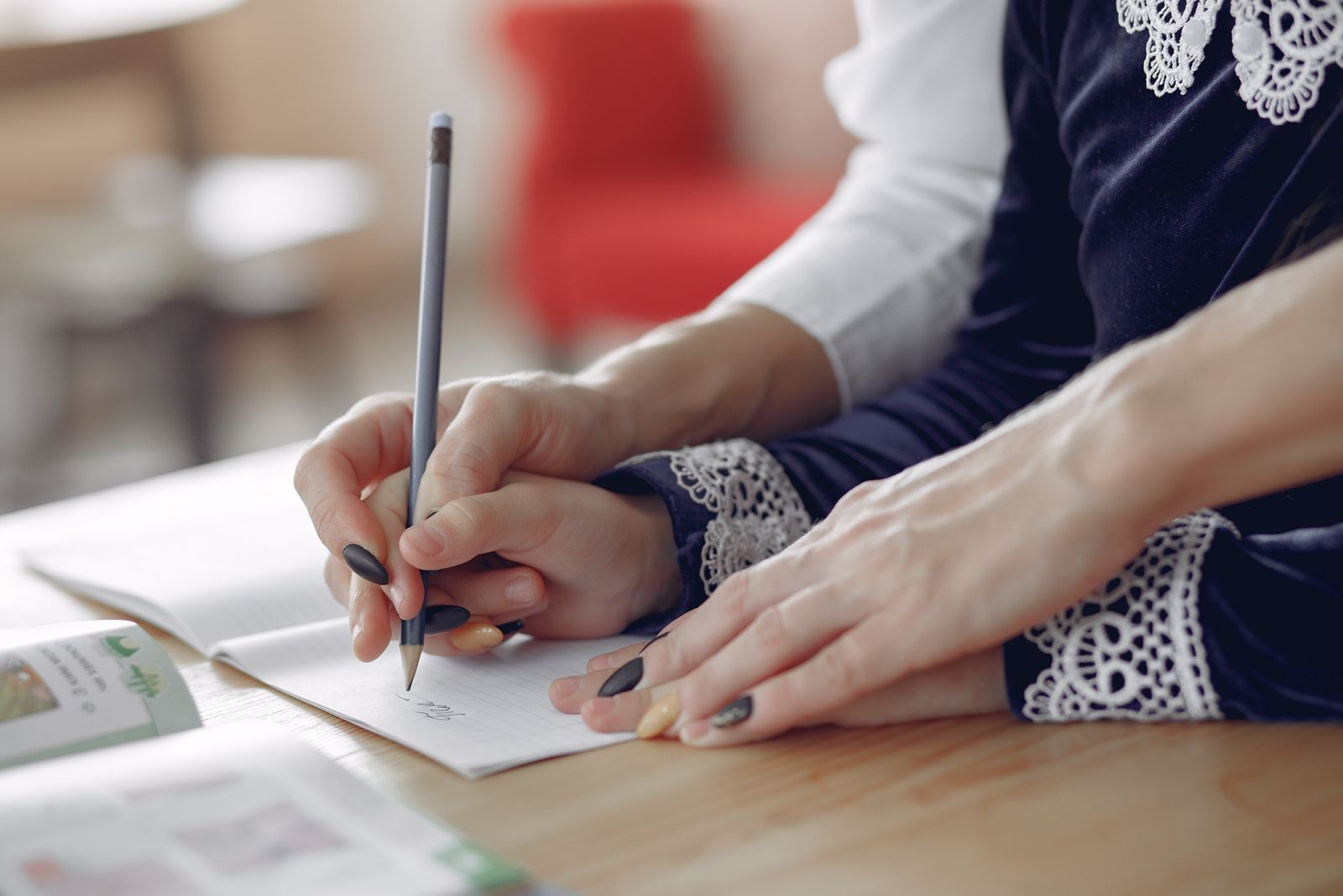 An adult's hand guiding a pupil's pencil in an exercise book