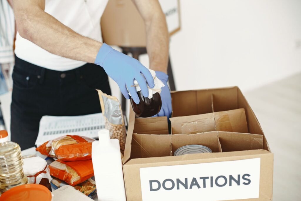 Gloved hands packing tins into a cardboard donations box
