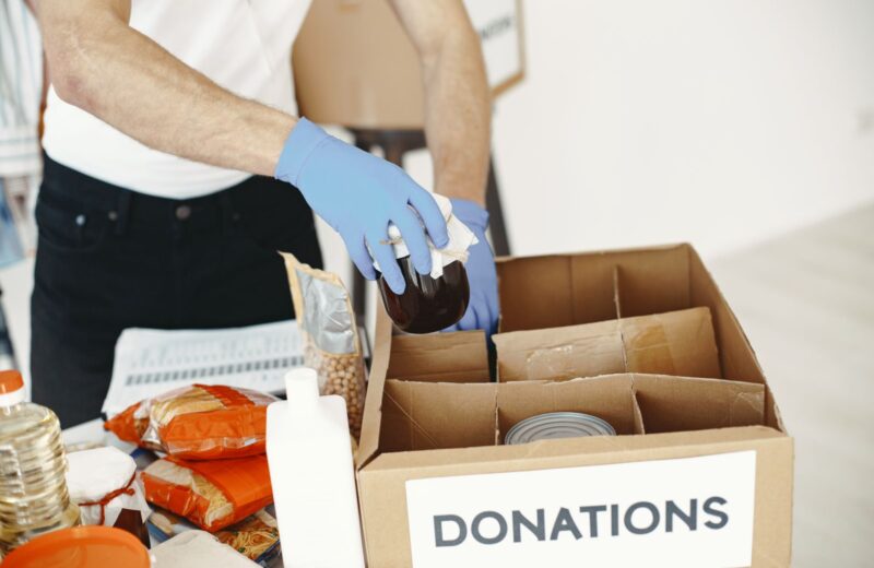 Gloved hands packing tins into a cardboard donations box