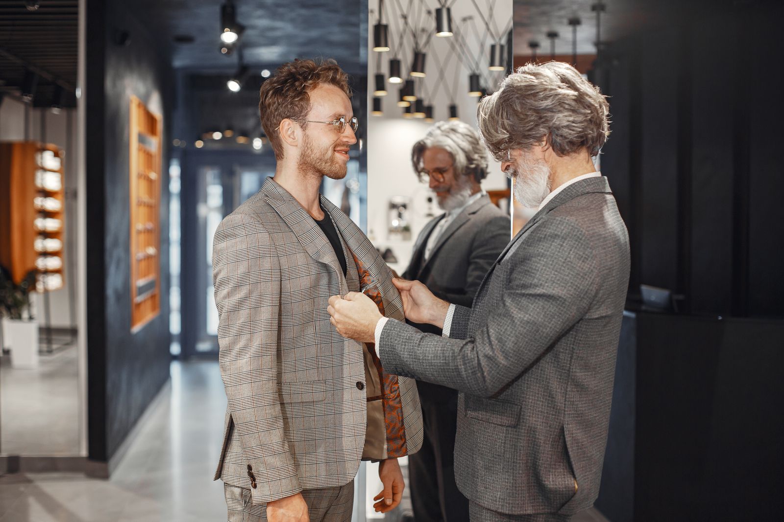 A tailor adjusting a customer's checked jacket at the shoulder in a menswear shop