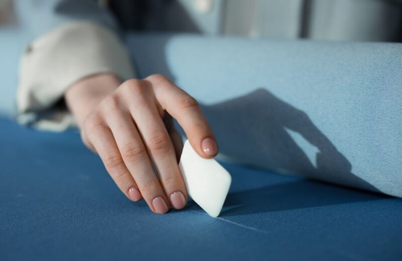 A hand drawing a line with tailor's chalk on blue cloth