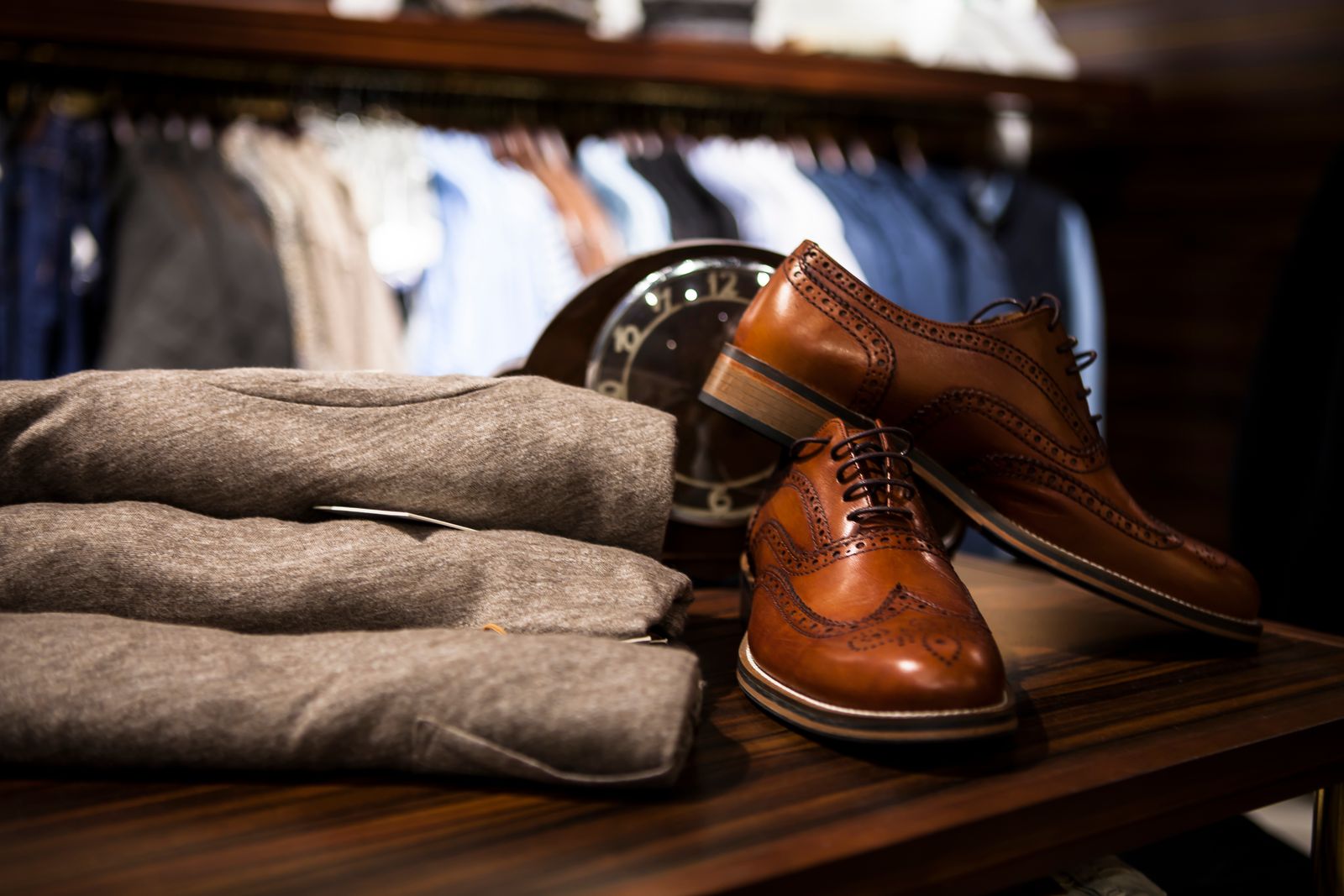 Tan leather brogues beside a stack of folded grey knitwear on a dark wooden shop table