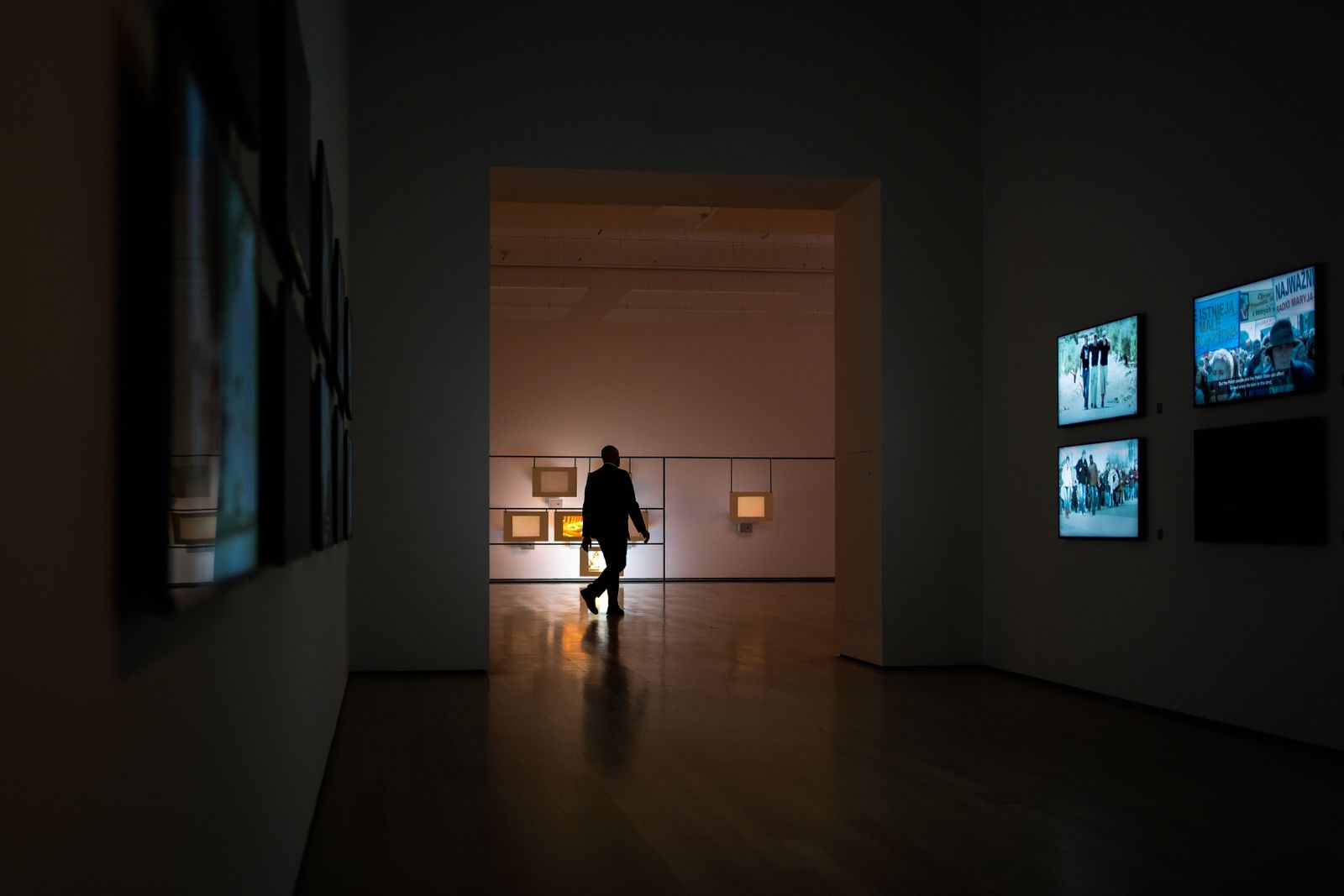 A silhouette walking through a dim gallery lined with illuminated screens