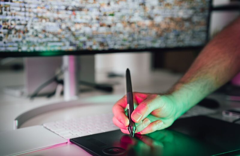 A digital artist drawing with a stylus on a graphics tablet in front of a monitor