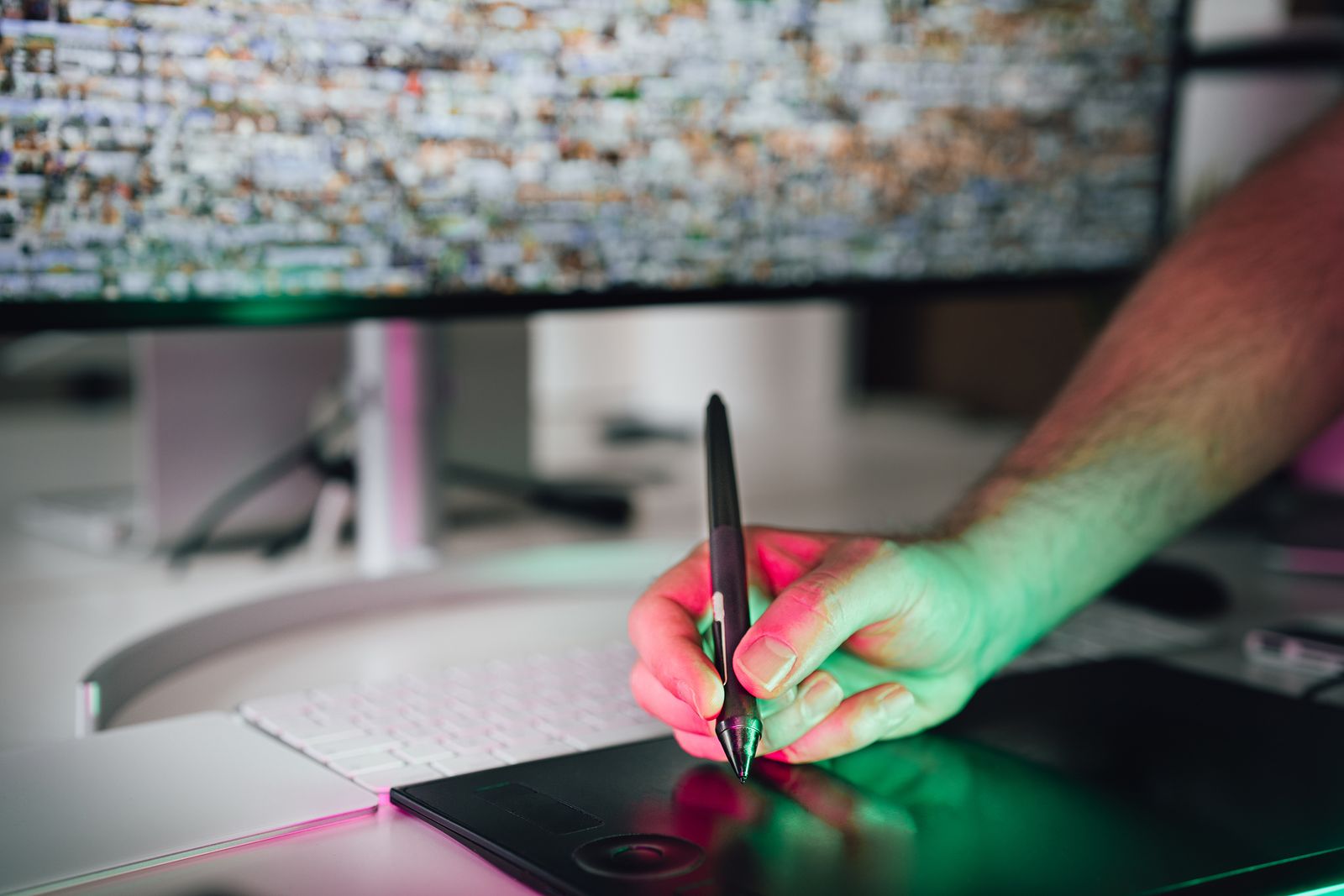 A digital artist drawing with a stylus on a graphics tablet in front of a monitor
