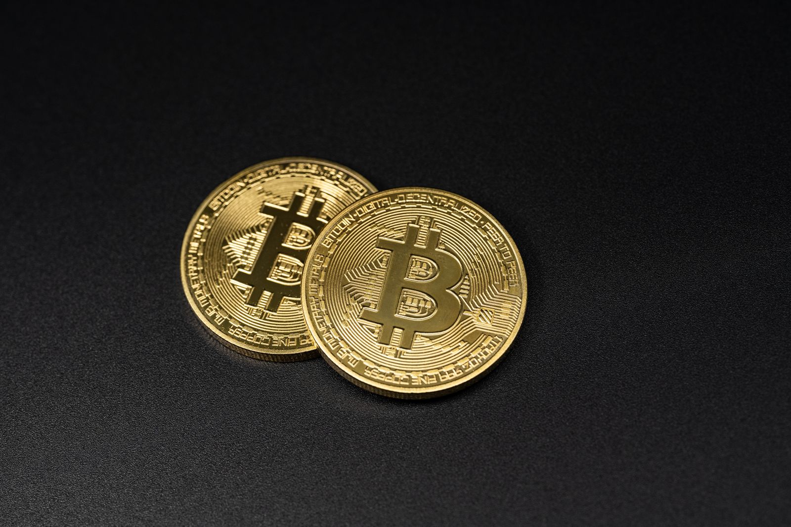 Two gold-coloured Bitcoin coins resting on a black surface