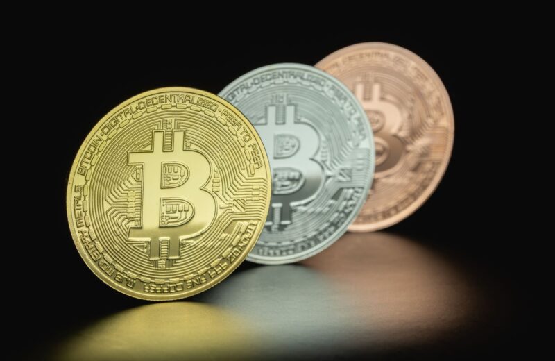 Three Bitcoin coins in gold, silver and bronze tones against a dark background