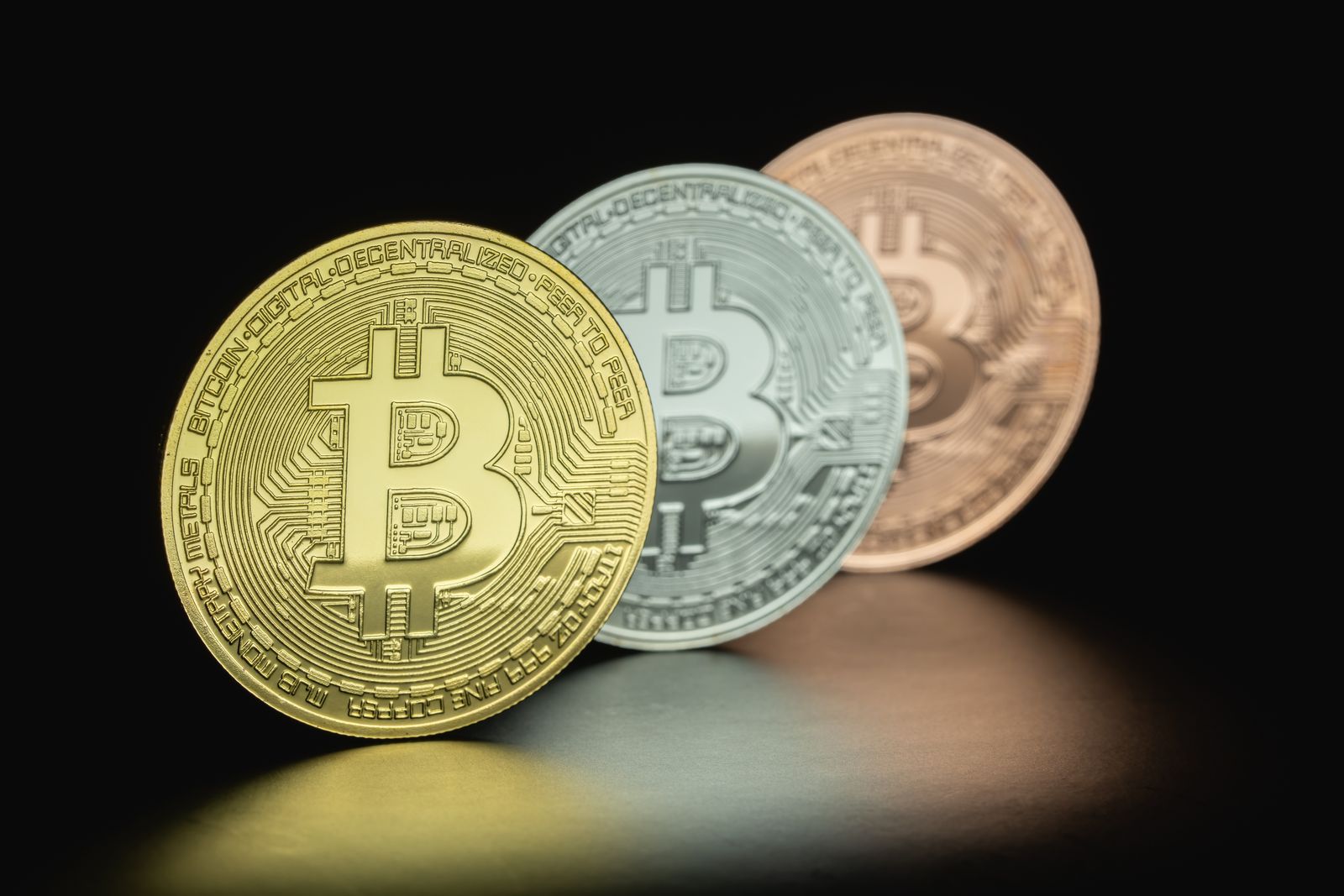 Three Bitcoin coins in gold, silver and bronze tones against a dark background