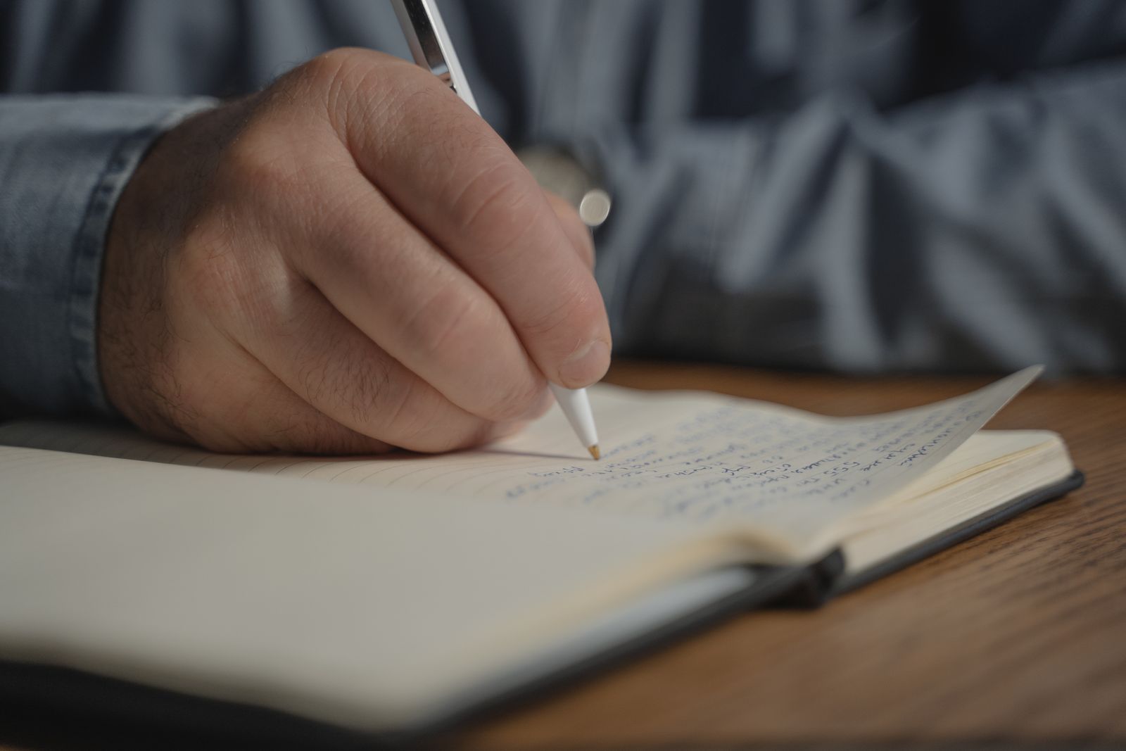 A hand writing with a pen in an open notebook on a wooden desk
