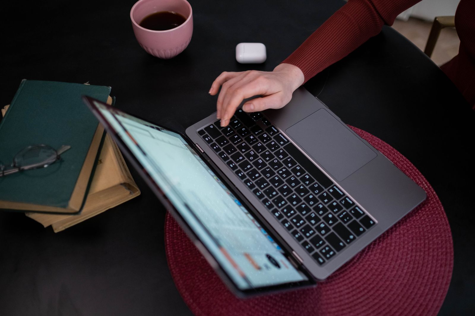 A person typing on a laptop beside a coffee cup and a stack of books
