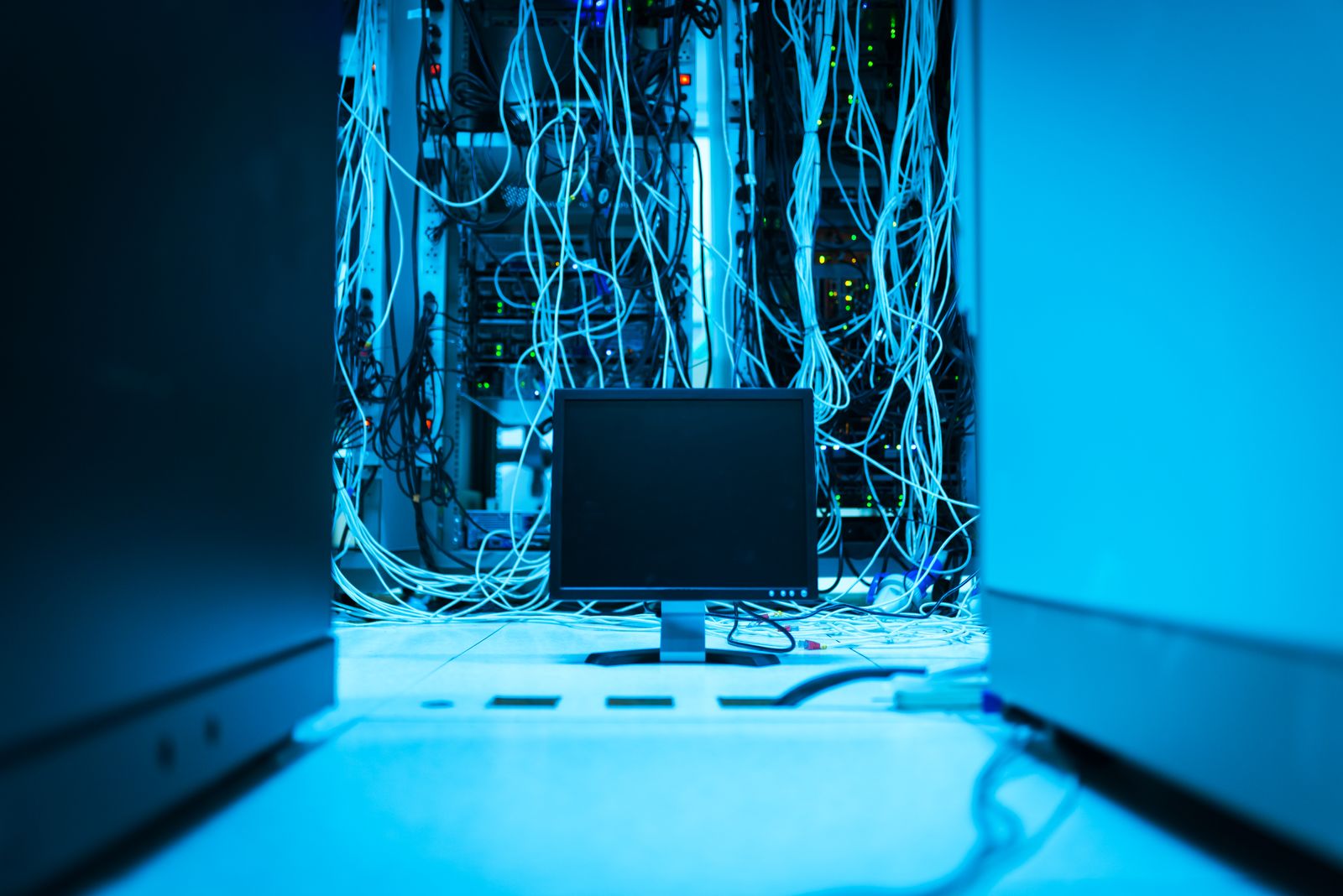 A server room lit in cyan, with cables hanging behind a single monitor