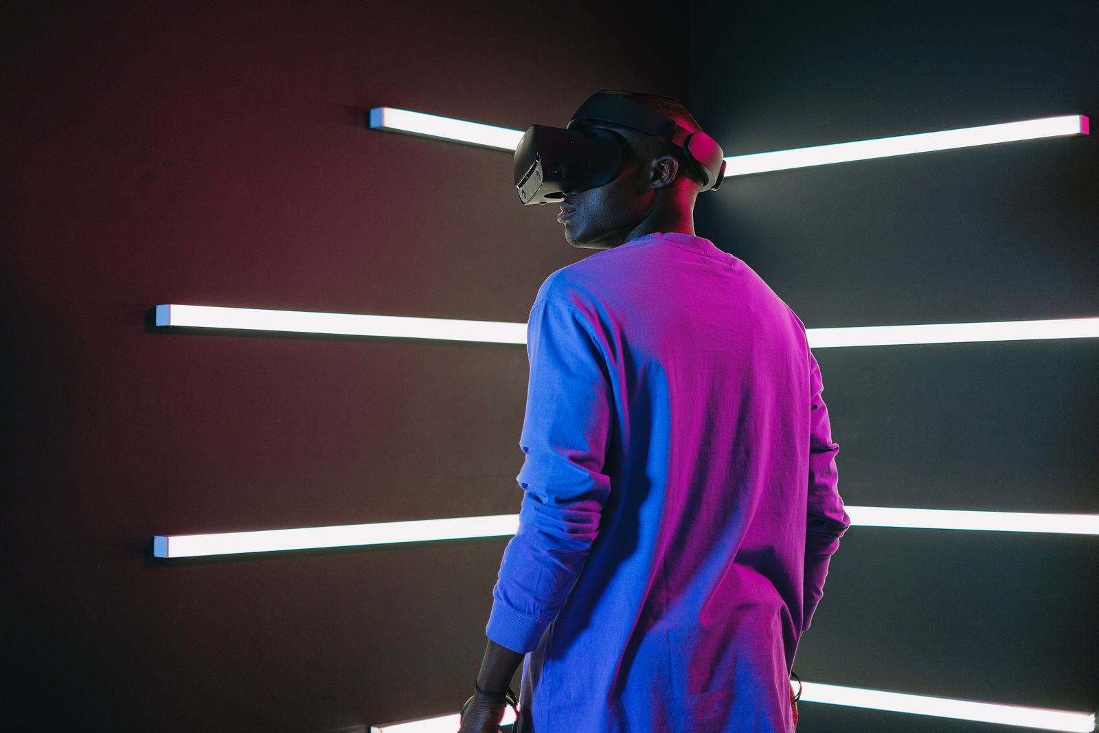 A person seen from behind wearing a VR headset in a corridor of white light strips