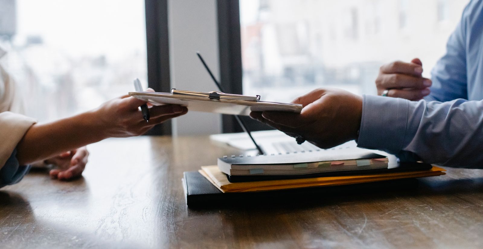 A clipboard with papers handed across a desk during a hiring meeting