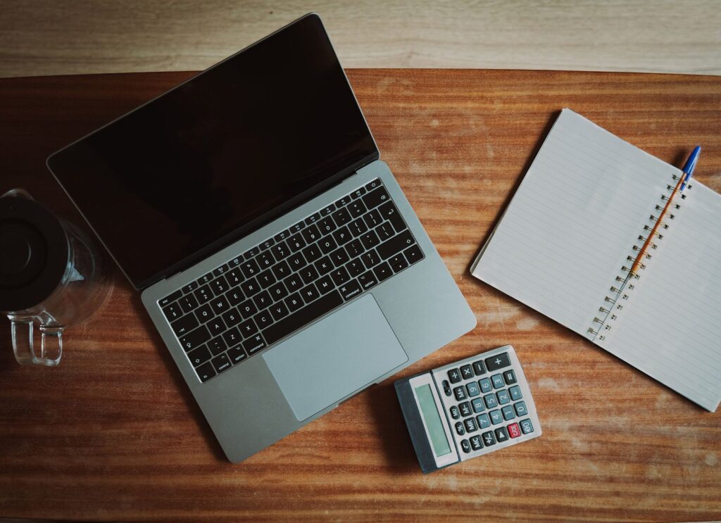 A laptop, a calculator and an open notebook on a wooden desk