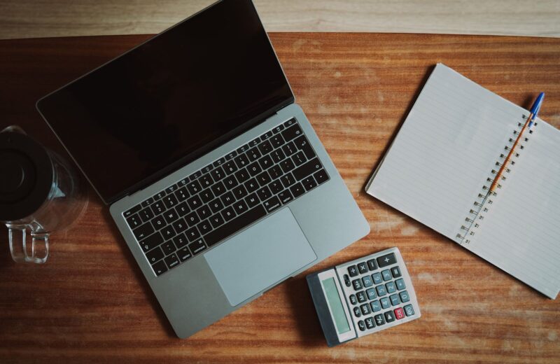 A laptop, a calculator and an open notebook on a wooden desk