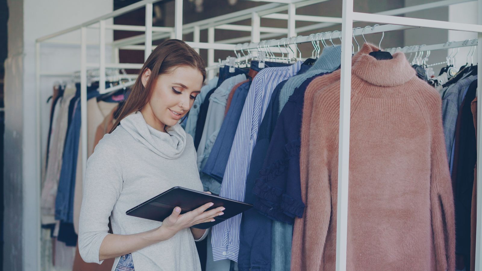 A shop assistant checking stock on a tablet between clothing rails