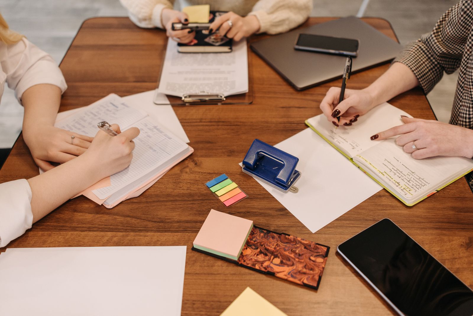Three people at a wooden table planning with notebooks, papers and sticky notes