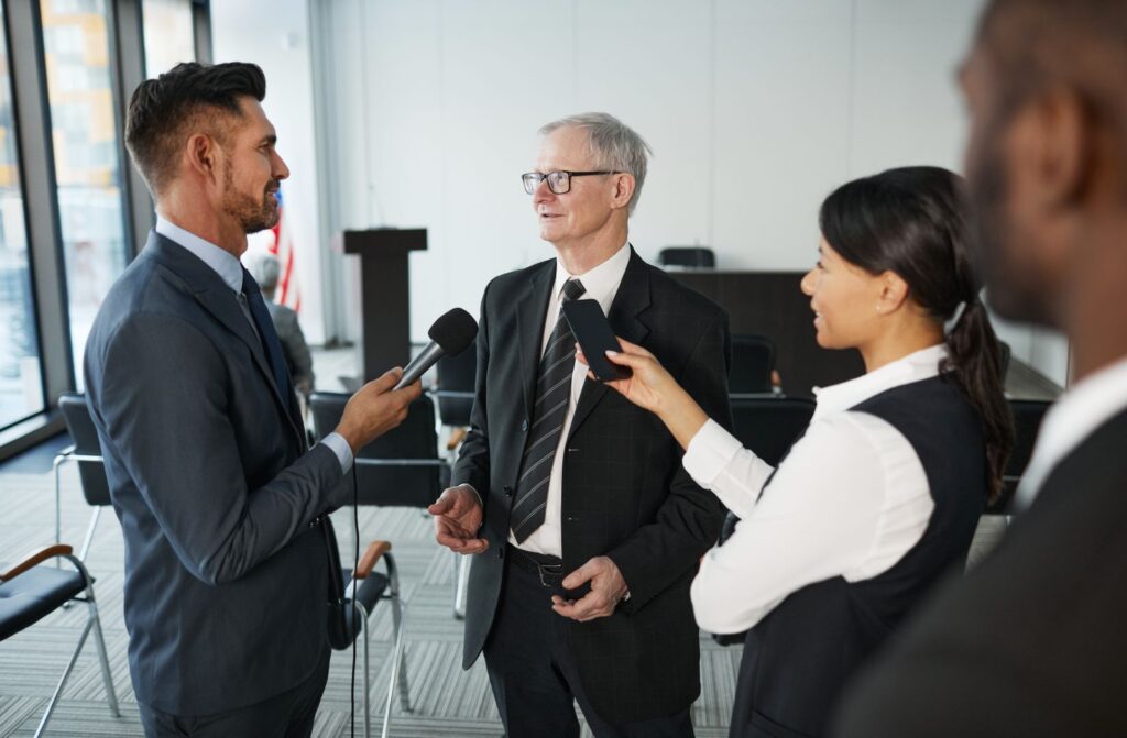 Journalists holding microphones towards a man in a suit during an interview