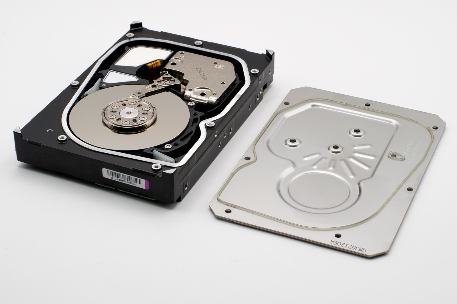 An opened hard drive beside its removed cover plate