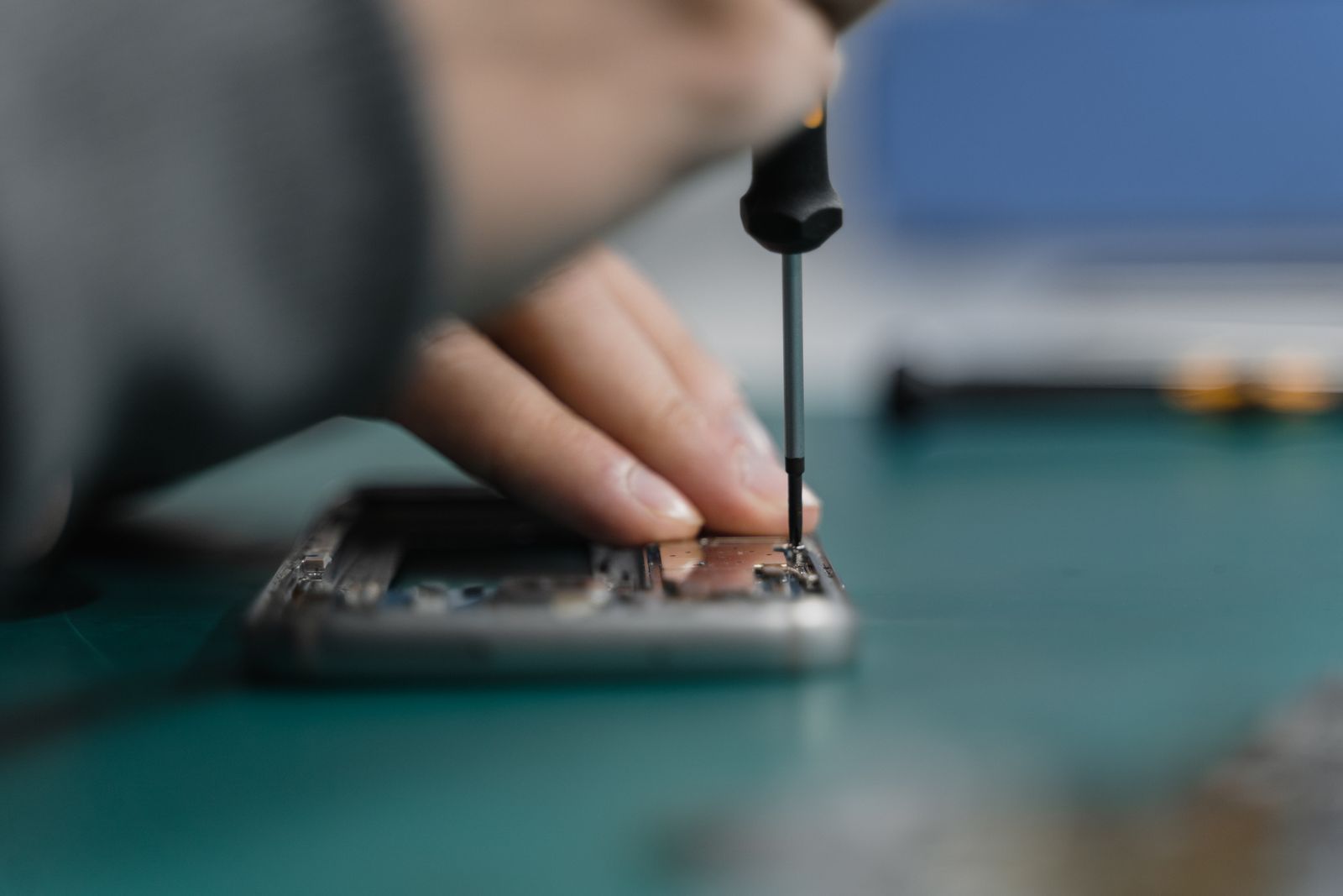 A technician's hand turning a precision screwdriver on an opened phone