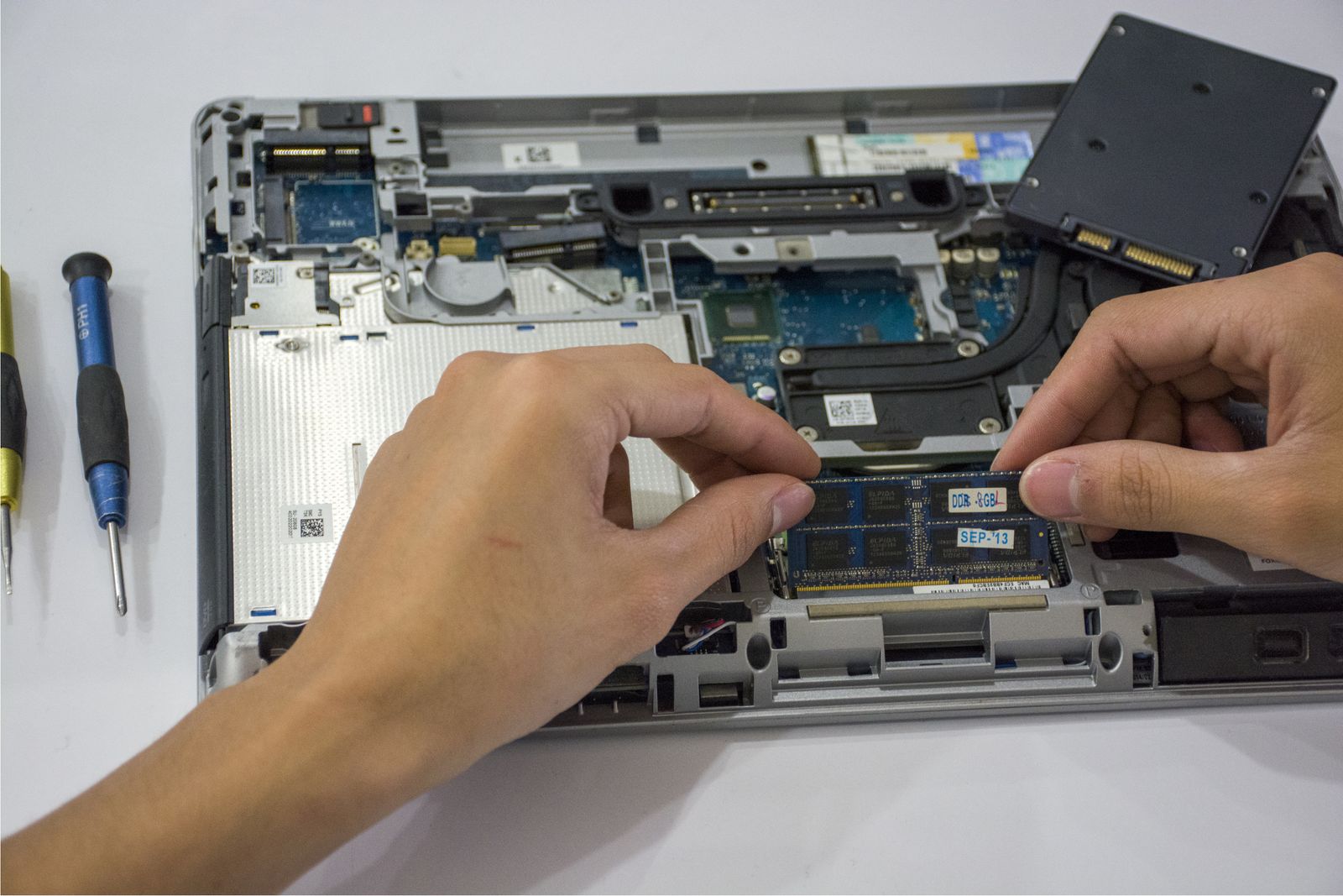 Hands fitting a part inside an opened laptop on a white bench