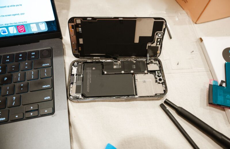 An opened phone with its battery visible, next to repair tools and a laptop