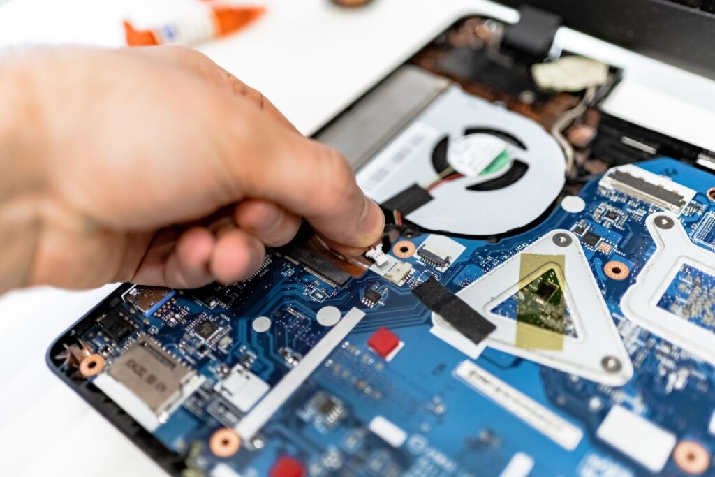 A hand with a screwdriver over a laptop's board and cooling fan