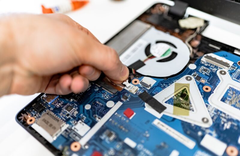 A hand with a screwdriver over a laptop's board and cooling fan