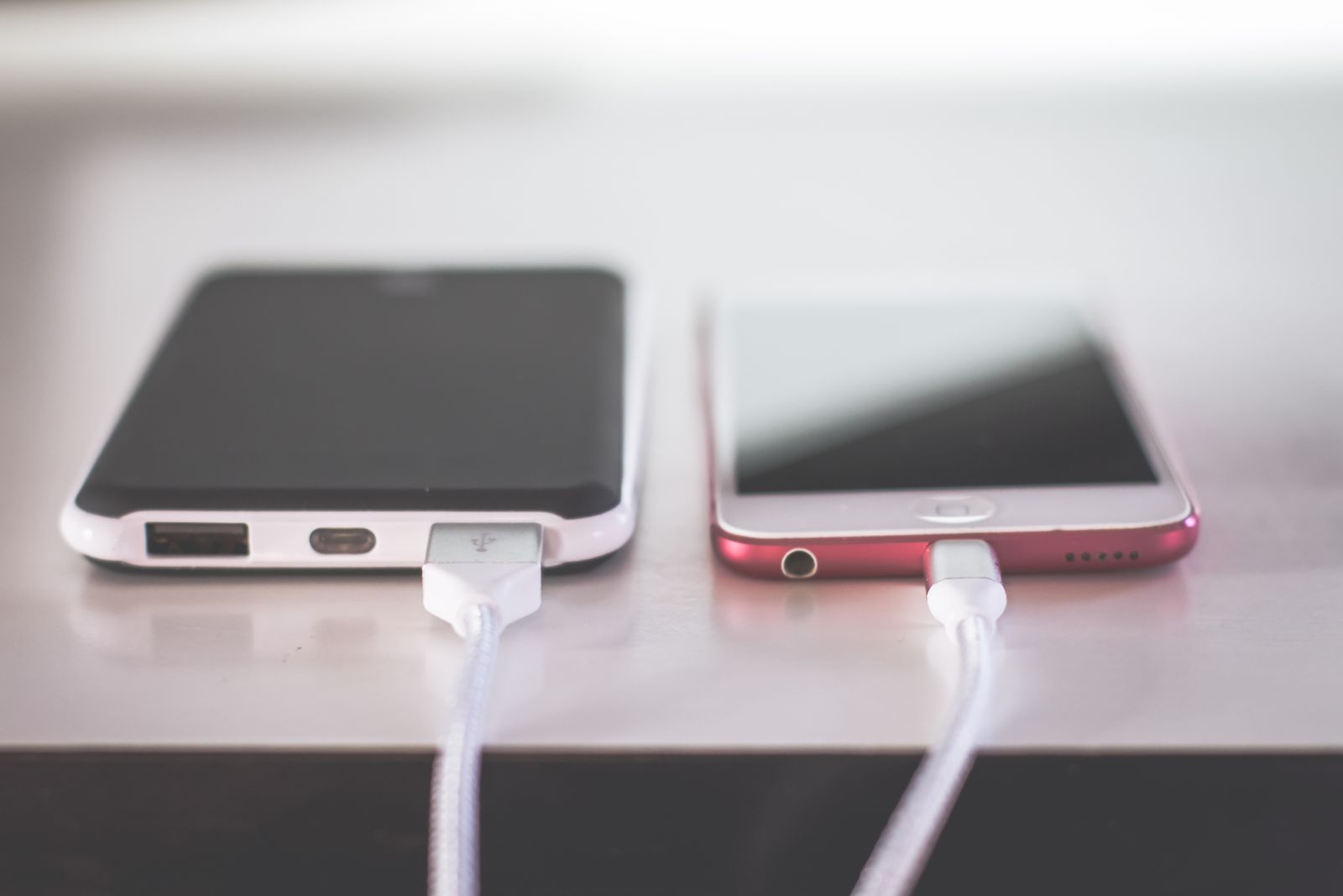 Two phones charging side by side on a light desk