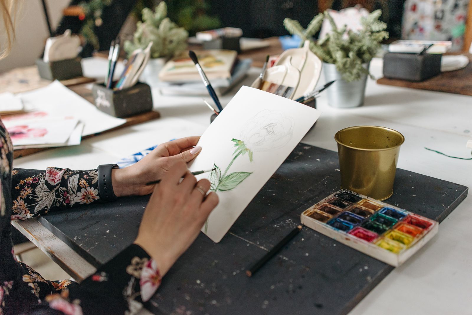 An illustrator painting a botanical watercolour on paper at a desk with brushes