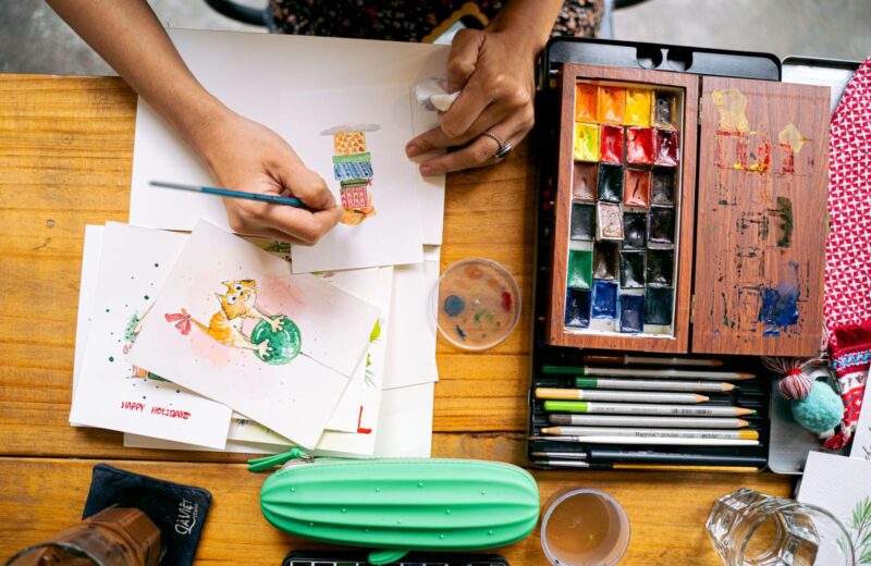 A watercolour painting in progress seen from above, with a palette and brushes