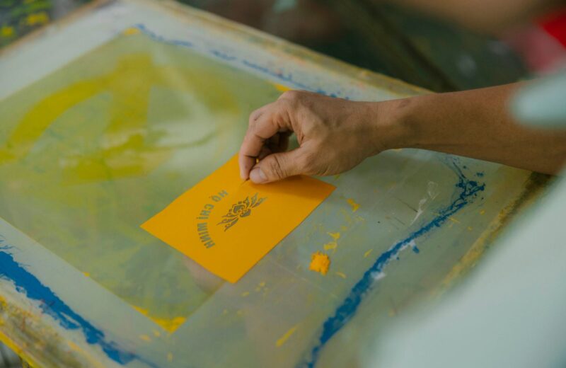A hand lifting a freshly printed yellow card from a screen
