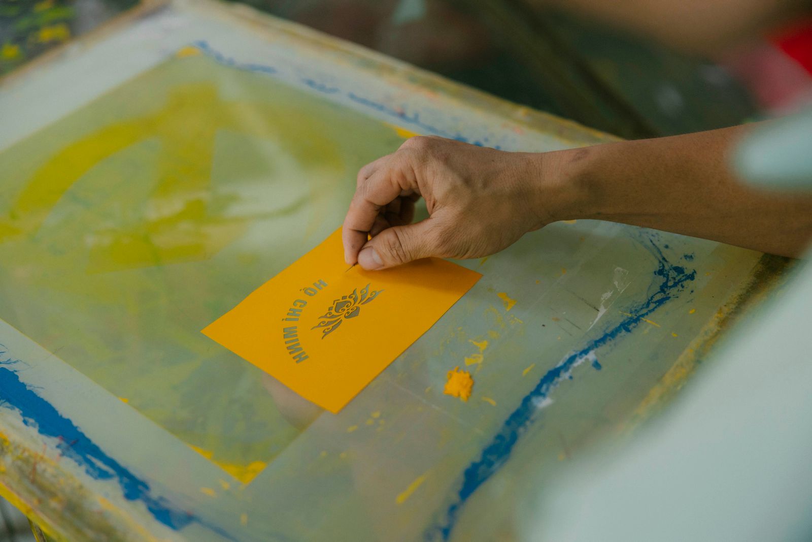 A hand lifting a freshly printed yellow card from a screen