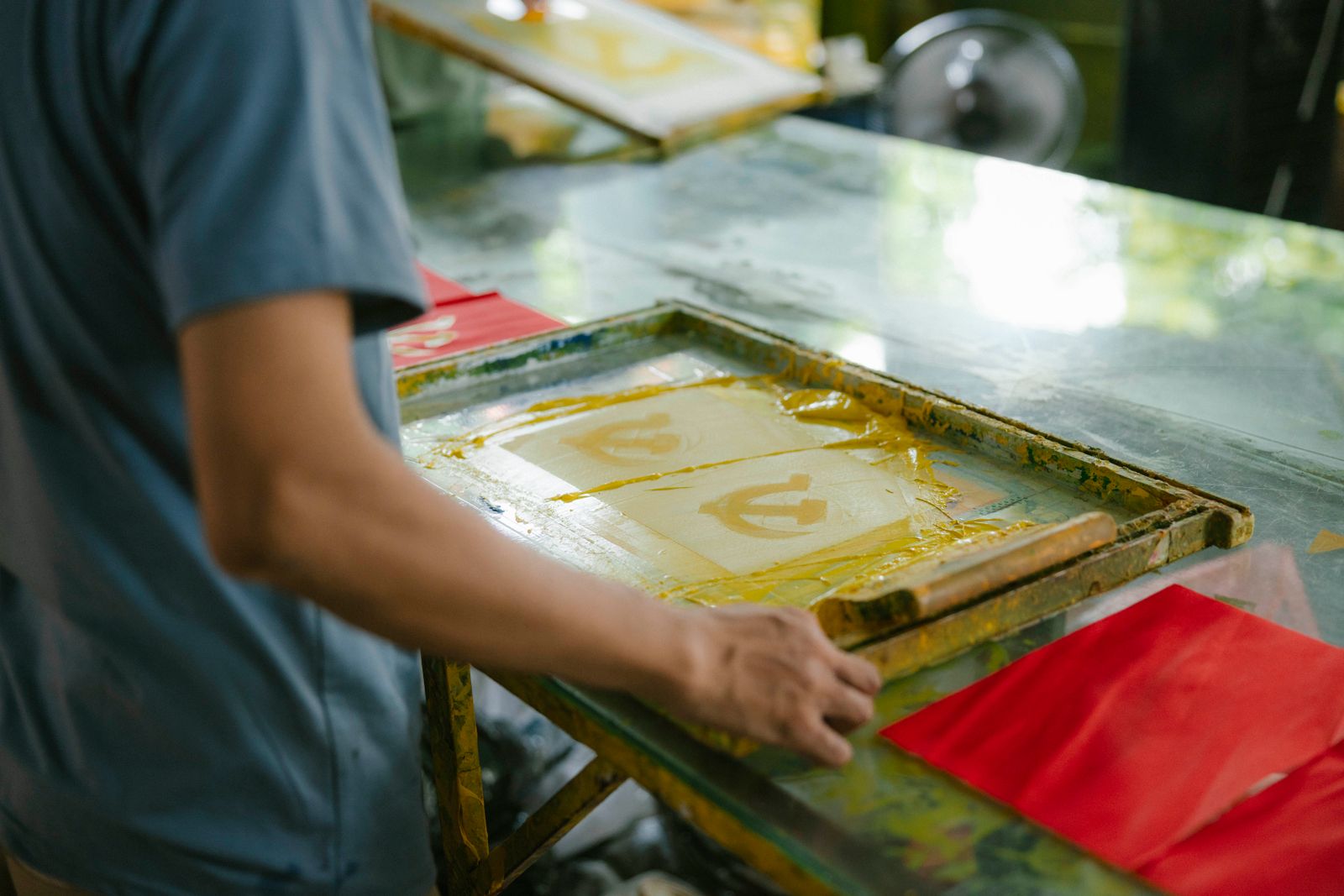 Hands pulling a print through a silkscreen frame in a print studio