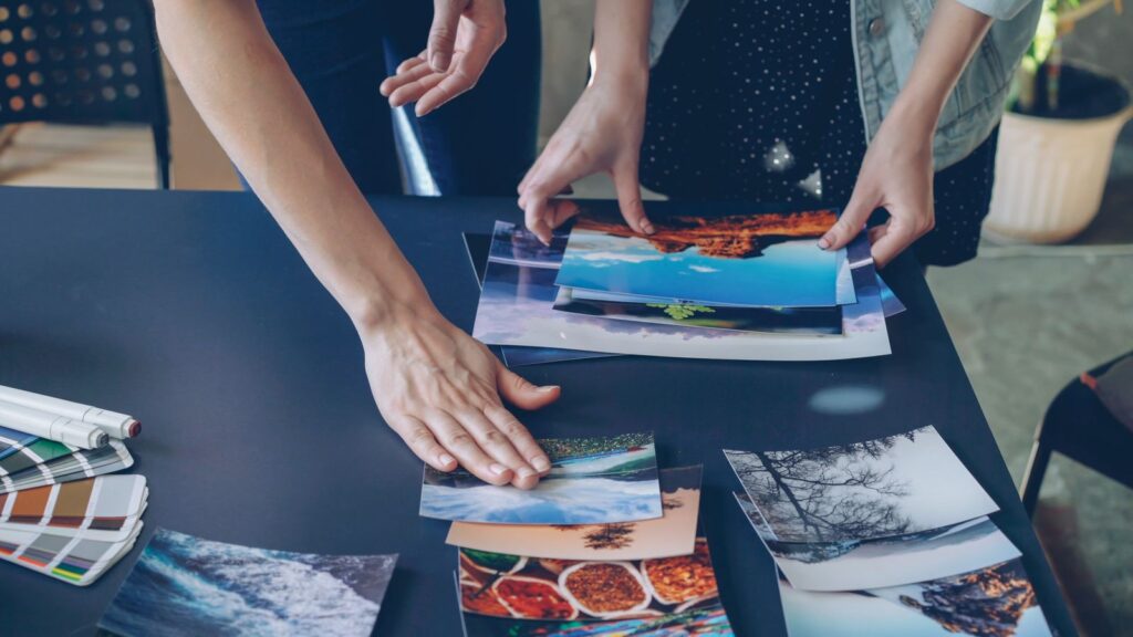 Two people sorting printed photographs on a dark table