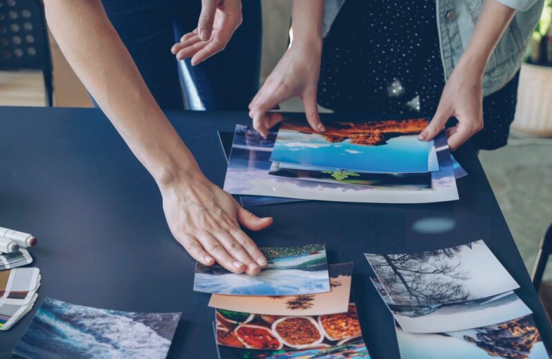 Two people sorting printed photographs on a dark table