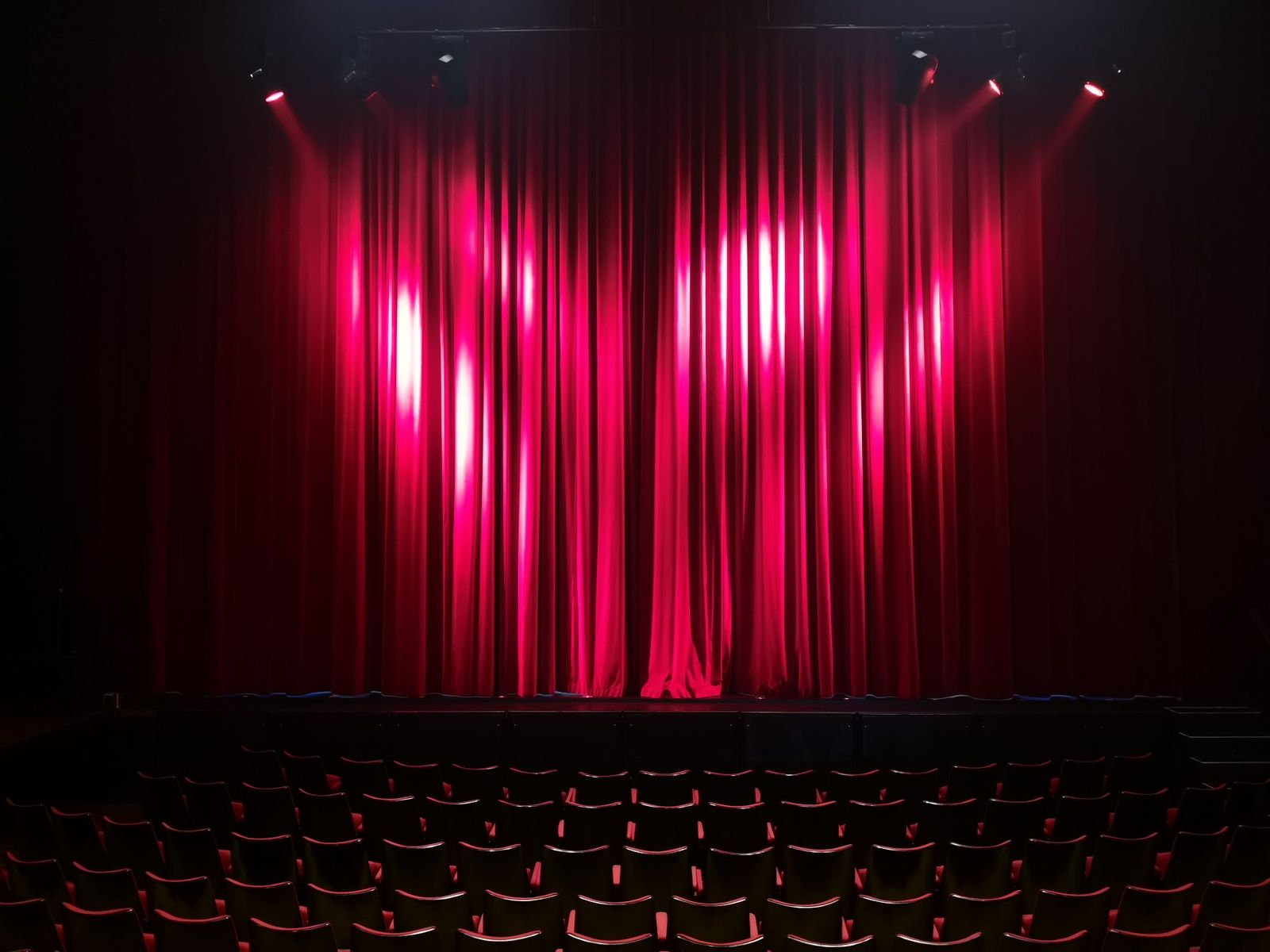 An empty stage with red curtains seen from the seats