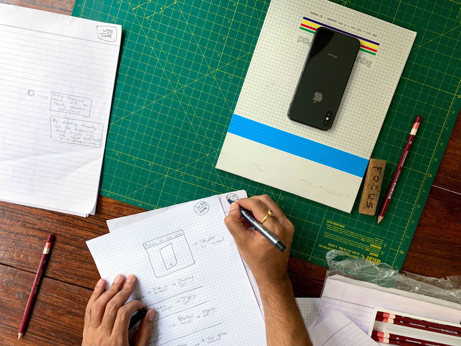 A designer drawing page wireframes on squared paper beside a phone and pencils
