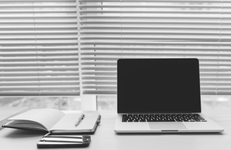 A black and white desk with a laptop, an open notebook and a phone