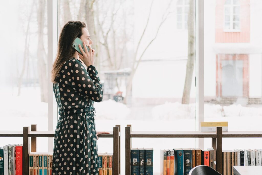 A woman talking on her phone by tall windows in a library