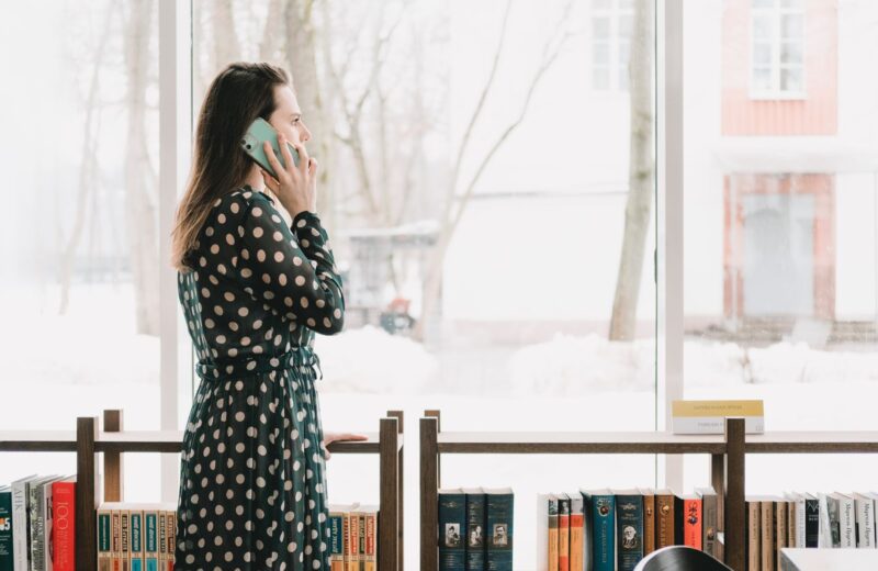 A woman talking on her phone by tall windows in a library