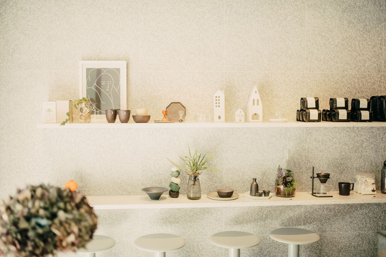 A white shop wall with two long shelves of ceramics, candles and small prints