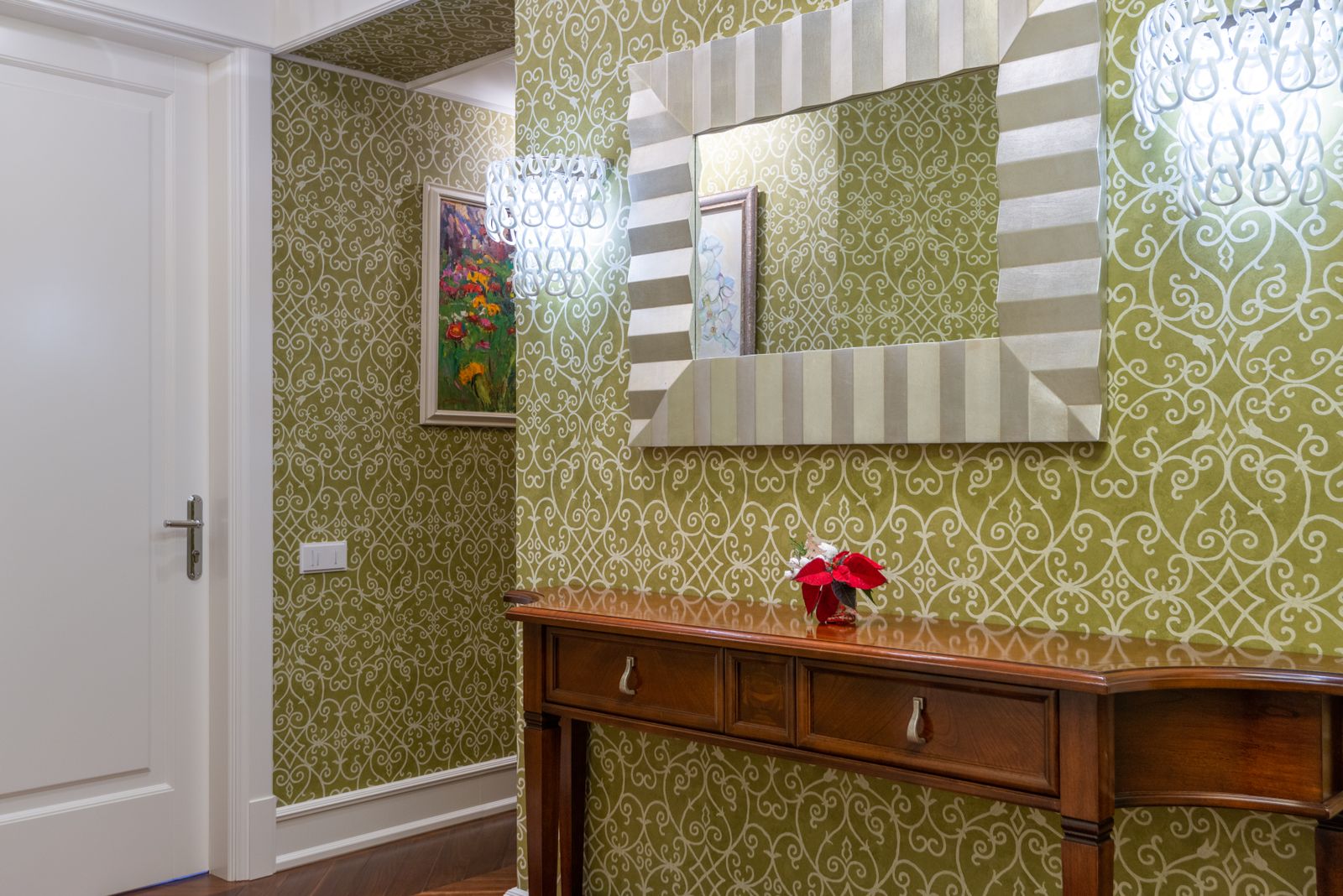 A hallway with patterned wallpaper, a wooden console table and a large framed mirror