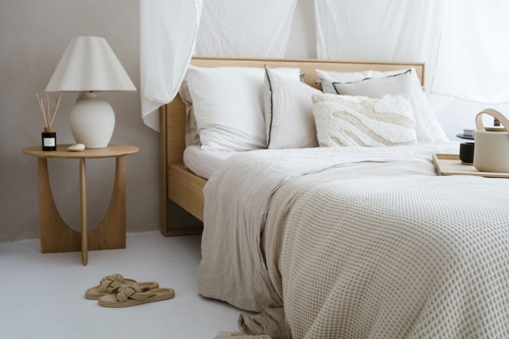 A neutral bedroom with linen bedding, a small side table and a soft lamp