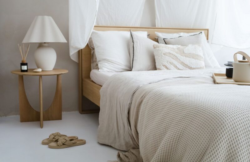 A neutral bedroom with linen bedding, a small side table and a soft lamp