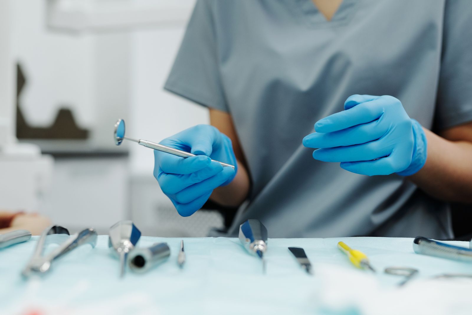 A dentist's gloved hands holding a mirror and a probe over the instrument tray