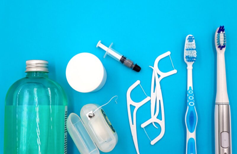 Toothbrushes, floss picks and mouthwash laid out on a blue surface