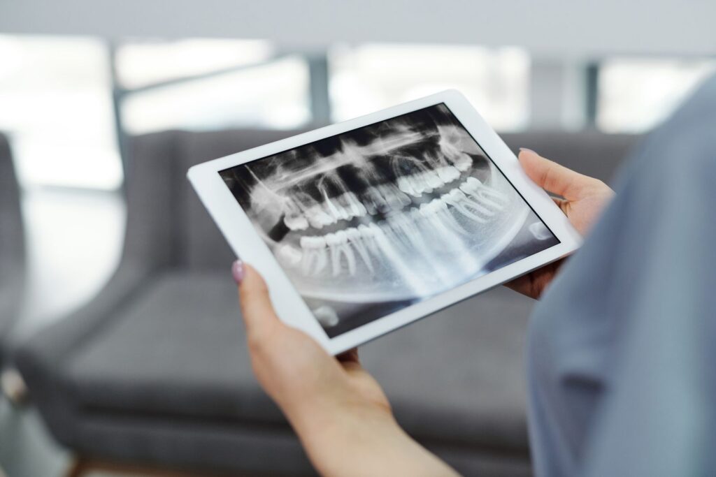 Hands holding a tablet with a dental X-ray, the practice blurred behind