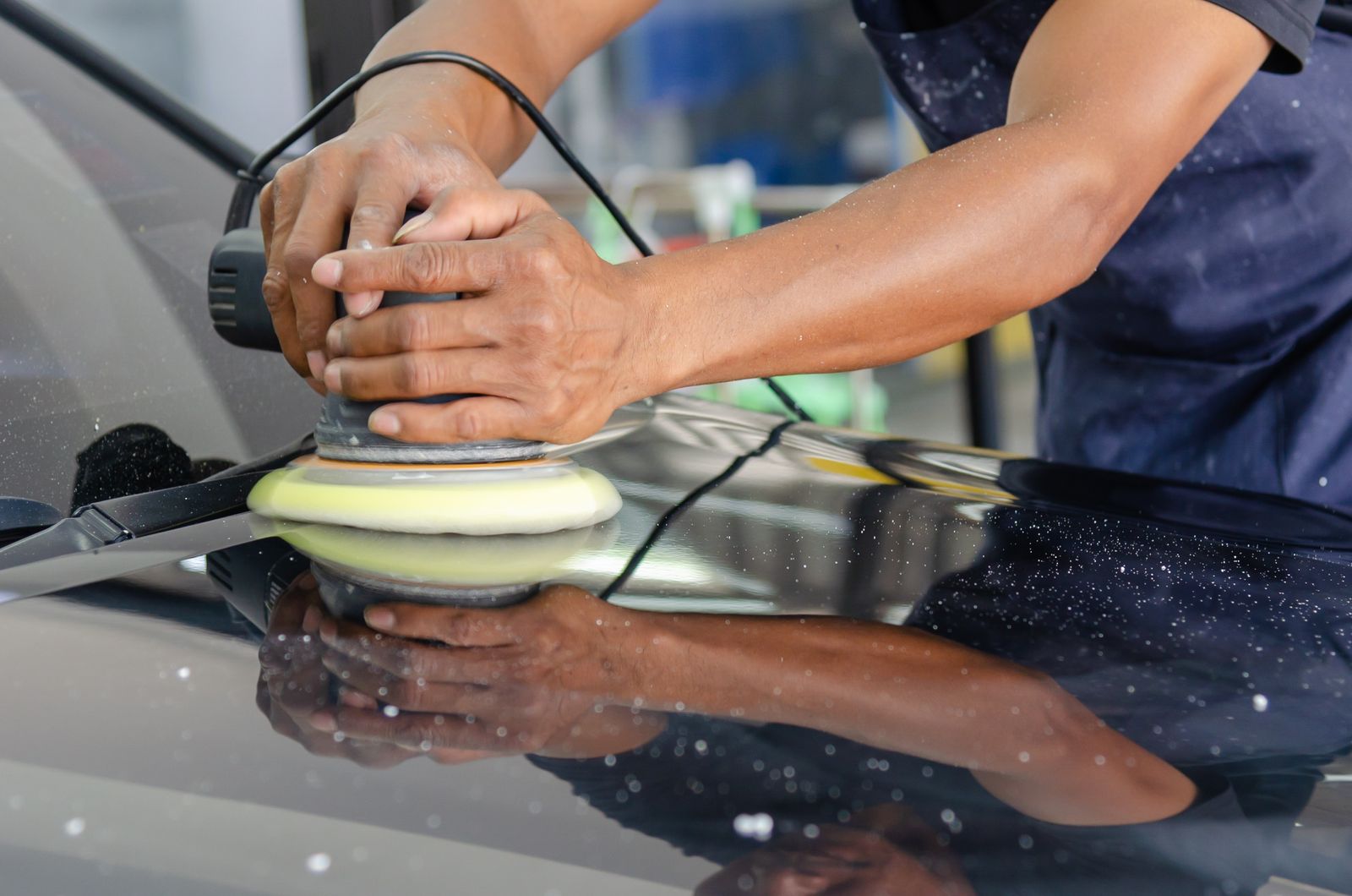 Hands holding a dual-action polisher with a yellow foam pad on a dark bonnet