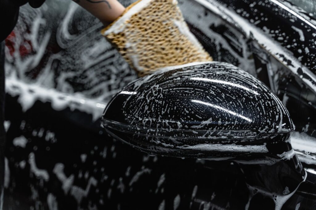 A wash mitt with foam on a black wing mirror